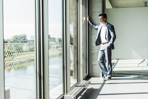 Geschäftsmann am Fenster stehend, mit Händen in den Taschen - UUF11273