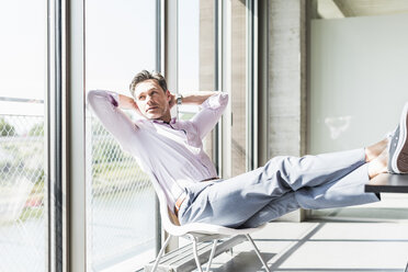 Businessman sitting at desk with feet up, looking out of window - UUF11281