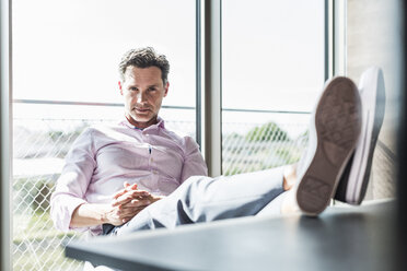 Businessman sitting at desk with feet up, looking at camera - UUF11282