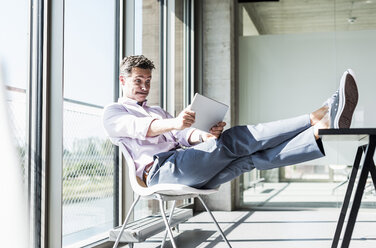 Businessman sitting at desk with feet up, looking shocked at digital tablet - UUF11286