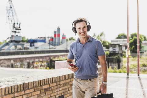 Geschäftsmann beim Spaziergang in der Stadt, mit Smartphone und Kopfhörern, lizenzfreies Stockfoto