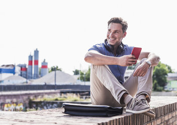 Businessman sitting on a wall, using smartphone - UUF11290