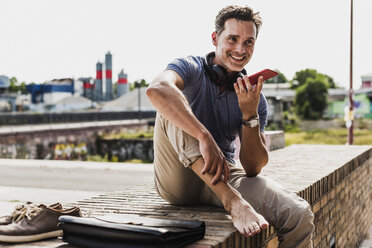 Businessman sitting on a wall, using smartphone - UUF11291