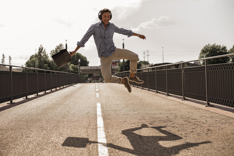 Geschäftsmann mit Kopfhörern und Aktentasche springt vor Freude auf einer Straße, lizenzfreies Stockfoto