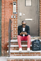 USA, NYC, Brooklyn, Mann wartet auf der Treppe, benutzt Smartphone - JUBF00226