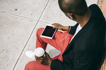 Mann, der auf der Straße sitzt, ein digitales Tablet benutzt und Kaffee trinkt - JUBF00229