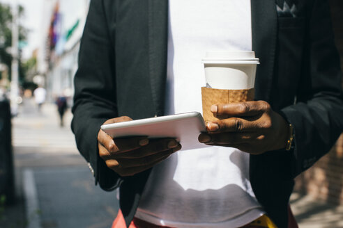 USA, NYC, Brooklyn, Mann geht auf der Straße, hält eine Tasse Kaffee und ein digitales Tablet - JUBF00237