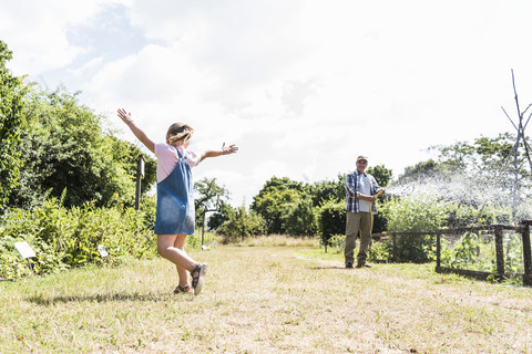 Carefree girl in garden with grandfather watering plants stock photo