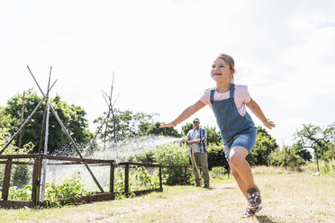 Carefree girl in garden with grandfather watering plants - UUF11330