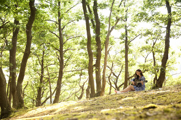 Young woman playing guitar in forest - MFRF00938