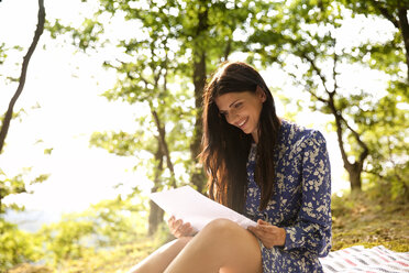 Lächelnde junge Frau im Wald, die einen Brief liest - MFRF00939