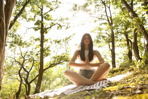 Young woman sitting on blanket in forest practicing yoga stock photo