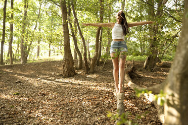 Junge Frau im Wald balanciert auf einem Baumstamm - MFRF00956