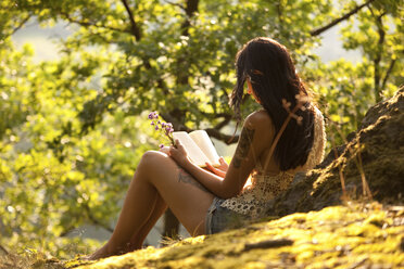 Junge Frau im Wald hält Blumen und liest ein Buch - MFRF00966