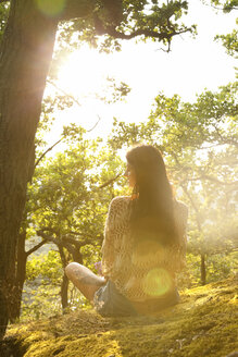Young woman sitting in forest at sunset - MFRF00970