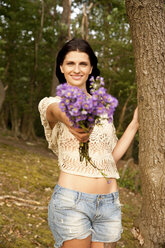 Porträt einer lächelnden jungen Frau mit Blumenstrauß im Wald - MFRF00974