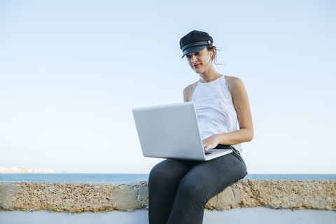 Junge Frau mit Hut benutzt einen Laptop im Freien, lizenzfreies Stockfoto