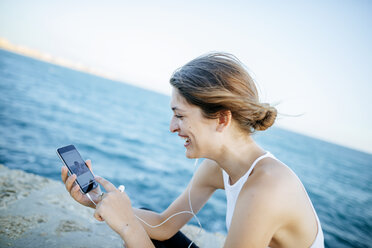 Junge Frau schaut sich Fotos auf dem Smartphone am Meer an - KIJF01682