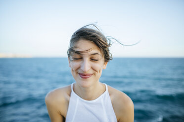 Junge Frau lächelnd mit geschlossenen Augen mit Meer Hintergrund - KIJF01683