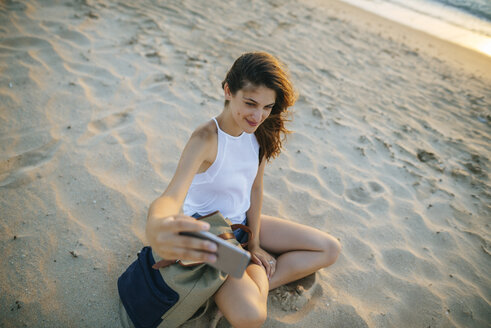 Junge Frau macht ein Selfie mit einem Smartphone am Strand - KIJF01687