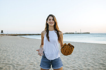 Junge Frau spielt mit Baseballhandschuh am Strand bei Sonnenuntergang - KIJF01690