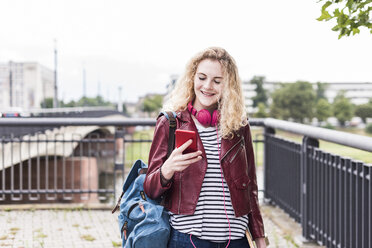 Porträt einer lächelnden jungen Frau, die auf ihr Mobiltelefon schaut - UUF11344