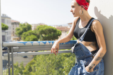 Tattooed young woman standing on balcony looking at distance - FMOF00311