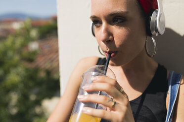 Portrait of young woman with headphones drinking soft drink - FMOF00312