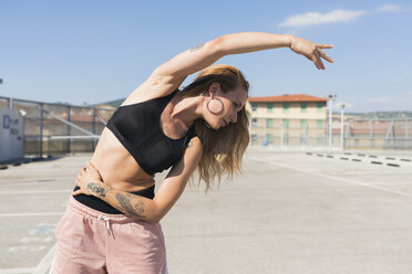 Tattooed young woman doing stretching exercises - FMOF00318