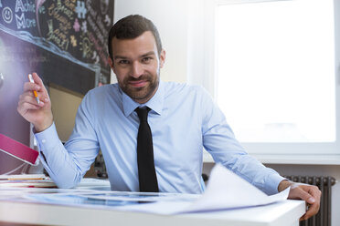 Portrait of confident businessman at desk in creative office - FKF02470