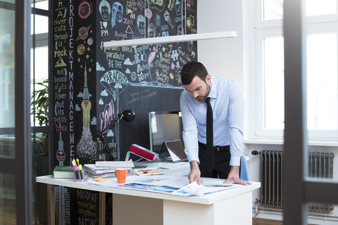 Geschäftsmann am Schreibtisch im Büro und betrachtet Ausdrucke, lizenzfreies Stockfoto