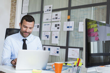 Businessman in office using laptop at desk - FKF02485