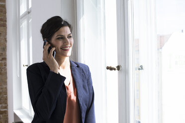 Smiling businesswoman on the phone at the window - FKF02499