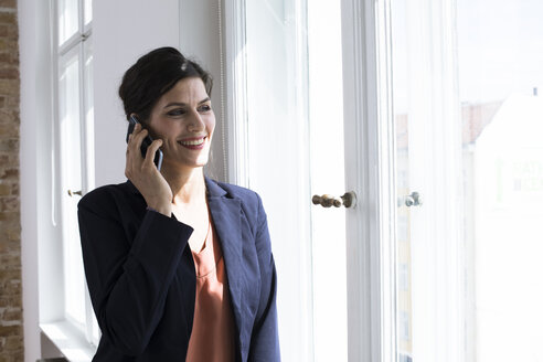 Lächelnde Geschäftsfrau beim Telefonieren am Fenster - FKF02499