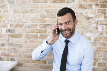 Porträt eines lächelnden Geschäftsmannes am Telefon vor einer Backsteinmauer - FKF02508