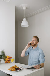 Laughing businessman on the phone at breakfast table at home - MOMF00195
