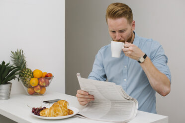 Businessman drinking coffee while reading newspaper in the morning at home - MOMF00196