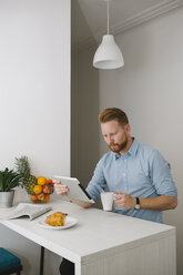 Businessman drinking coffee while using tablet at home - MOMF00197