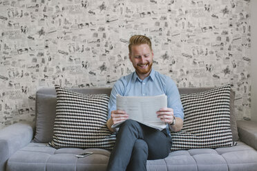 Lächelnder Geschäftsmann, der auf der Couch in seinem Wohnzimmer Zeitung liest - MOMF00201