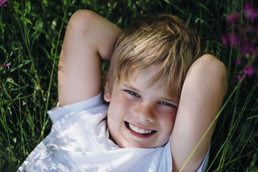 Porträt eines lächelnden kleinen Jungen, der sich auf einer Wiese im Garten entspannt - MJF02128