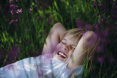 Lachender kleiner Junge auf der Wiese im Garten liegend - MJF02129