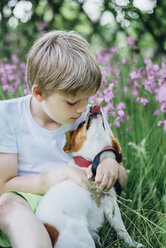 Kleiner Junge sitzt mit seinem Hund auf einer Wiese im Garten - MJF02131