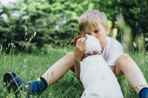 Kleiner Junge sitzt mit seinem Hund auf einer Wiese im Garten, lizenzfreies Stockfoto