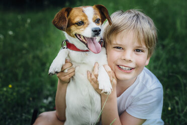 Porträt eines glücklichen kleinen Jungen mit seinem Hund auf einer Wiese im Garten - MJF02137