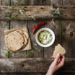 Hand with home-baked Naan bread and bowl of curd dip - EVGF03265