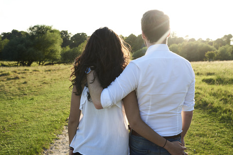 Rückenansicht eines jungen Paares Arm in Arm bei Sonnenuntergang, lizenzfreies Stockfoto