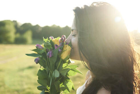 Profil einer jungen Frau, die bei Sonnenuntergang an einem Blumenstrauß riecht - IGGF00054