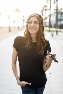 Lächelnde junge Frau an der Strandpromenade, die Musik hört - GIOF02989