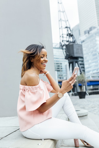 Lächelnde Frau, die mit ihrem Smartphone in der Stadt Nachrichten verschickt, lizenzfreies Stockfoto