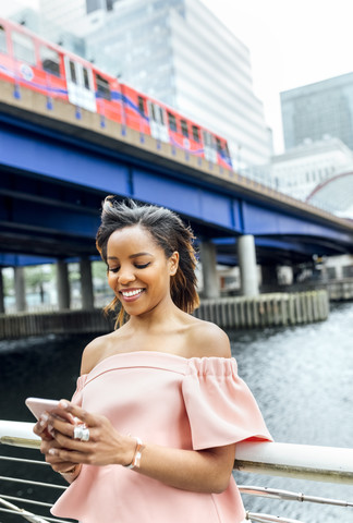 Lächelnde Frau, die mit ihrem Smartphone in der Stadt Nachrichten verschickt, lizenzfreies Stockfoto